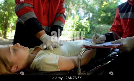 Paramedic doing CPR to girl, colleague making records, professionals saving life Stock Photo