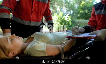 Paramedic examining woman on stretcher, colleague making record, rescue team Stock Photo