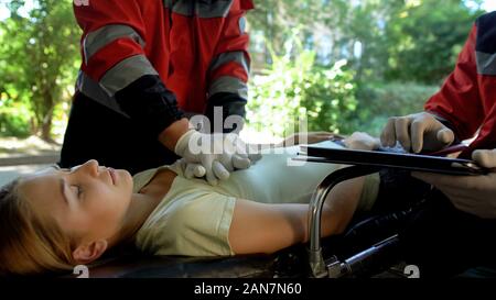 Male paramedic doing indirect heart massage, colleague using tablet for records Stock Photo