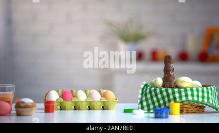 Dyed eggs in basket, chocolate bunny and paints on table, Easter preparation Stock Photo
