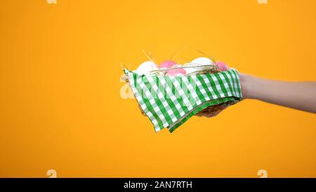 Female hand holding Easter basket on yellow background, festival celebration Stock Photo