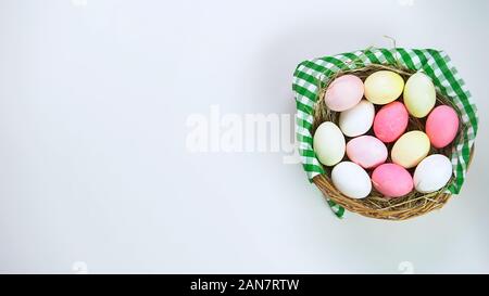 Basket of colored Easter eggs standing on white table, holiday celebration