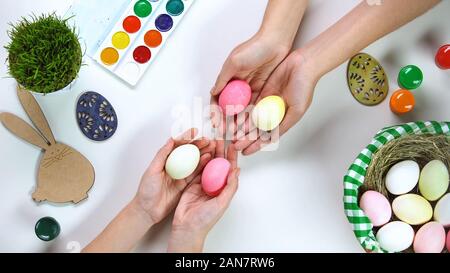 Dyed eggs in female hands, Easter bunny decoration and holiday basket on table Stock Photo