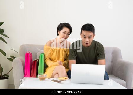 Excited Asian couple using laptop to purchase online with good deal. Stock Photo