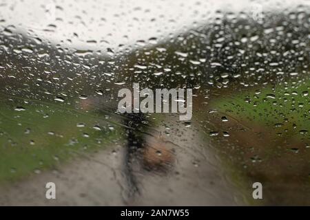 Silhouette of a woman holding a basket behind a raindrops on car glass surface Stock Photo