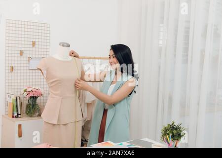 Young Asian female fashion designer taking measurements on mannequin in her studio Stock Photo