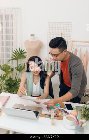 Designers team discussing fashion sketches, focused man and woman collaborating on new clothes collection creation choosing color working with swatche