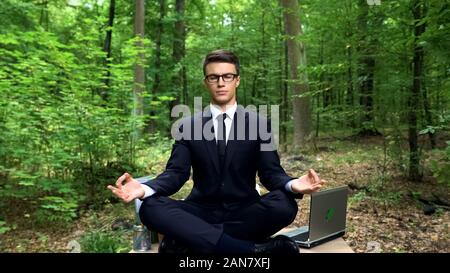 Businessman sitting on desk and meditating in fresh air in forest, inspiration Stock Photo