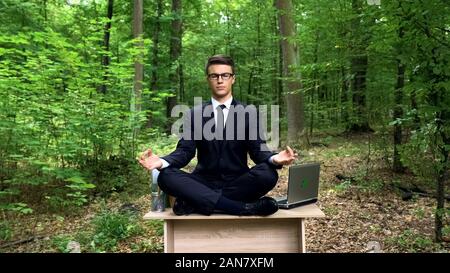 Happy businessman meditating in green forest, ability to cope with stress Stock Photo