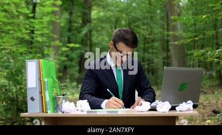 Creative young businessman writing down good ideas at desk in green forest Stock Photo