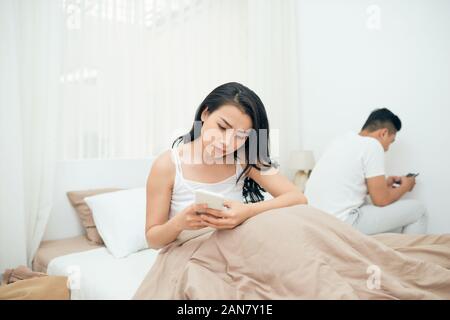 sad view of young married couple using their mobile phone in bed ignoring each other as strangers in relationship and communication problems Stock Photo