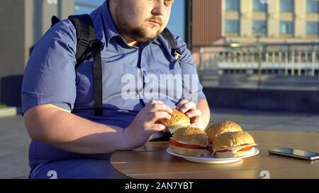 Overweight man holding hamburger, unhealthy nutrition, junk food, lifestyle Stock Photo