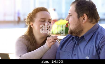 Girlfriend feeding boyfriend with salad, couple having lunch outside, city date Stock Photo