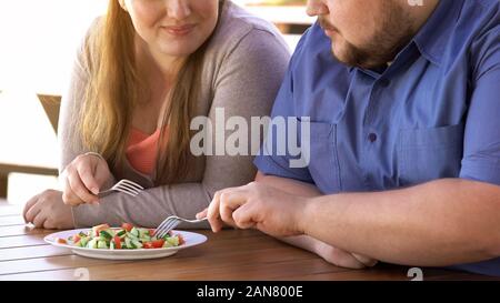 Plump couple eating fresh salad from one plate, weight loss, calories control Stock Photo