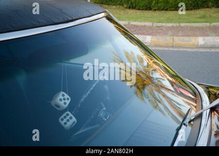 Front window detail of a purple classic american car at street. There are dice shaped retro style car ornament on rear view mirror and a palm tree ref Stock Photo