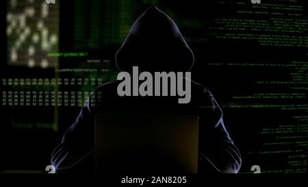 Hooded man working with computer code, hacking software, stealing private data Stock Photo