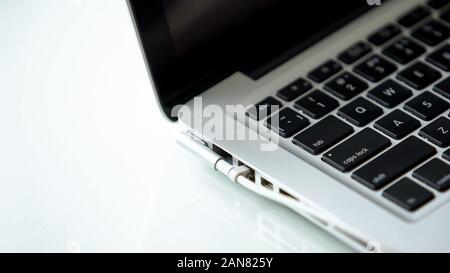 Power adapter plugged in laptop on white table, electric charger, technology Stock Photo