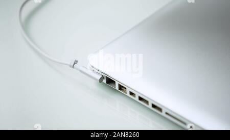 AC adapter plugged in closed laptop on white table, office workplace, gadget Stock Photo