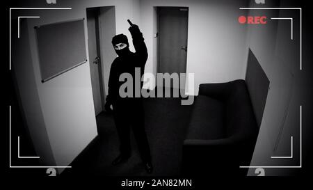 Dangerous criminal in balaclava showing middle finger at surveillance camera Stock Photo