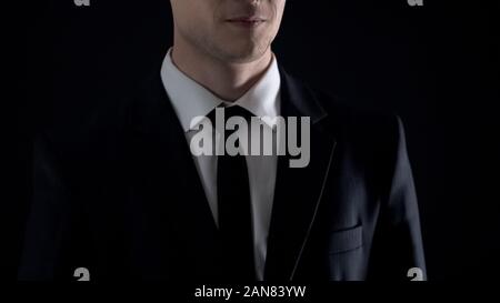 Man in suit smirking, isolated on black background, corruption and bribery Stock Photo