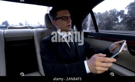 Thoughtful manager working on tablet, riding in luxury car using time in traffic Stock Photo