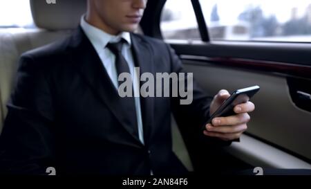 Young male in suit texting on smartphone while riding in personal business car Stock Photo
