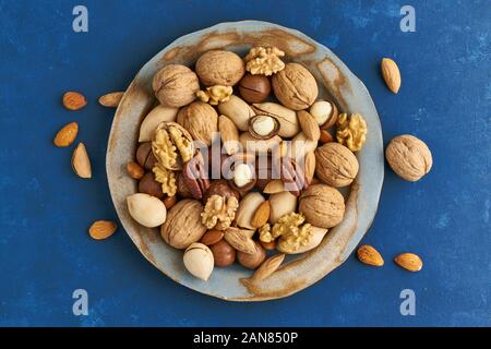 Classic blue in a food. Mix of nuts on plate - walnut, almonds, pecans, macadamia and knife for opening shell. Healthy vegan food. Clean eating, balan Stock Photo