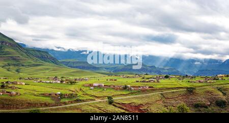 Panorama of a village in the mountains of Maloti Drakensberg Park with sunbeams breaking through the clouds and illuminating the green meadows, South Stock Photo