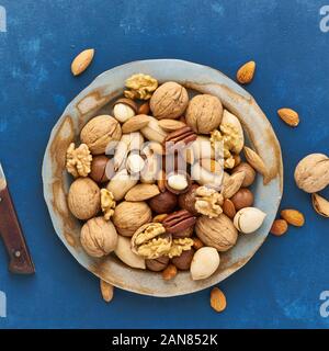 Classic blue in a food. Mix of nuts on plate - walnut, almonds, pecans, macadamia and knife for opening shell. Healthy vegan food. Clean eating, balan Stock Photo