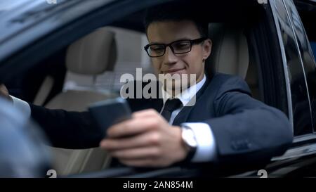 Glad businessman texting with girlfriend and smiling, sitting in car, smartphone Stock Photo