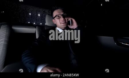 Cheerful man in suit talking on phone with girlfriend, sitting in car, way home Stock Photo