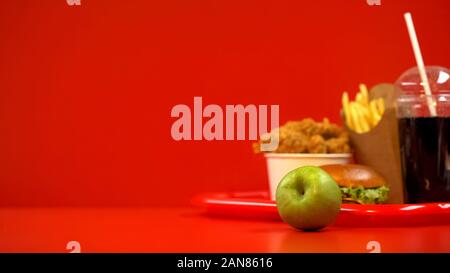 Green apple lying on table, fast food on background, choosing healthy nutrition Stock Photo