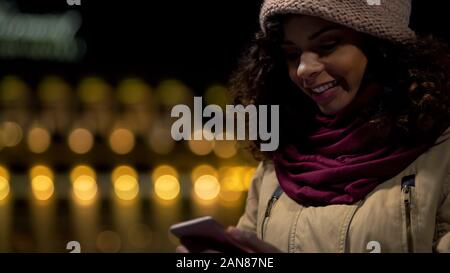 Happy biracial girl in good mood chatting in messenger with boyfriend, laughing Stock Photo