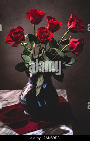 Dark setting of a bouquet of red roses in a vase on a table Stock Photo
