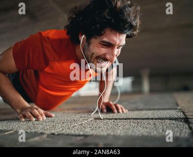 Young fit sporty man with serious face expression doing hard difficult plank fitness exercise or push ups on pavement