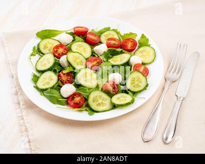Fresh salad with tomatoes, cucumbers, arugula, mozzarella. Oil with spices, side view, white background Stock Photo