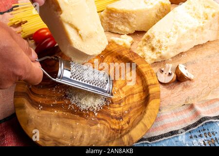 Man cooking with hard italian cheese, grated parmesan or grana padano cheese, hand with cheese grater Stock Photo