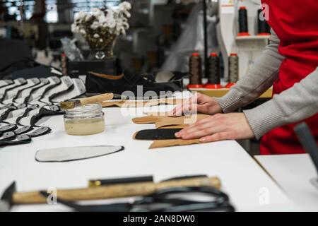 Shoemaker is adding glue with a brush to some pieces of leather that will be used to make shoes. The cobbler is working on his desk in his workshop. Stock Photo