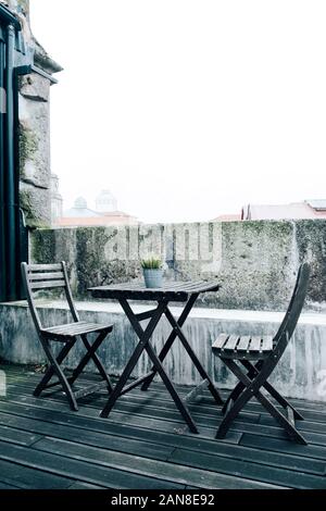 a view of a lonely roof terrace in the old town of Porto, in Portugal, set with an outdoor table and a pair of foldable chairs Stock Photo