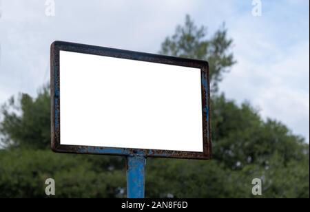 Metal sign template. Blank white board on blue rusty pole, nature trees background, copy space. Information signpost Stock Photo