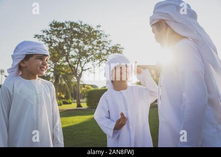 Children playing together in Dubai in the park. Group of kids wearing traditional kandura white dress from arab emirates Stock Photo