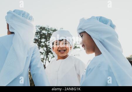 Children playing together in Dubai in the park. Group of kids wearing traditional kandura white dress from arab emirates Stock Photo