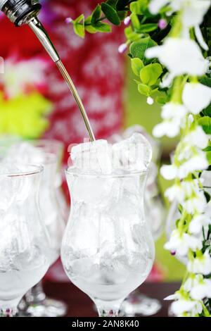 Syrup pouring in transparent glass full of ice, preparing cocktail Stock Photo