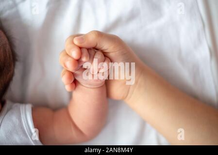 Closeup of a sister hand who hold the hand of one month little sister. Top view Stock Photo