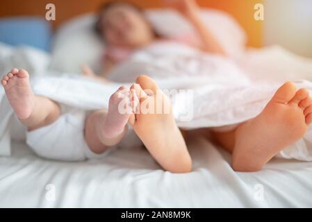 Tiny newborn's feet laying on the bed with elber sister or brother family sleep resting Stock Photo
