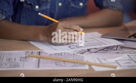 Mixed-race designer working on apartment layout plan, holding pencil, project Stock Photo