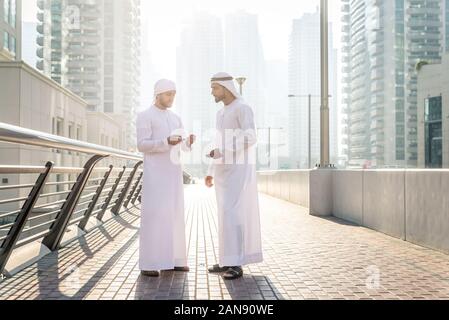 Two young businessmen going out in Dubai. Friends wearing the kandura traditional male outfit in Marina Stock Photo