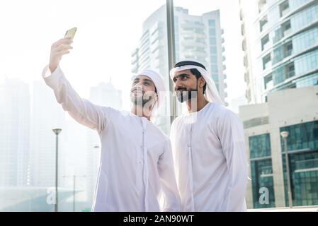 Two young businessmen going out in Dubai. Friends wearing the kandura traditional male outfit in Marina Stock Photo