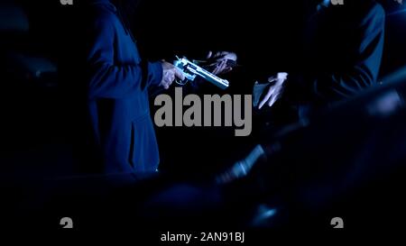 Teen robbing businessman at car park, threatening with gun, nighttime attack Stock Photo