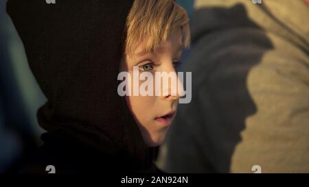 Lonely boy in hoodie sitting outdoor, bullying victim, humiliation at school Stock Photo